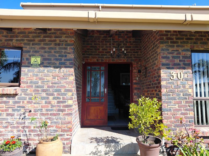 Front entrance of a face brick house featuring a timber door, tiled porch area, and clear house number signage.
