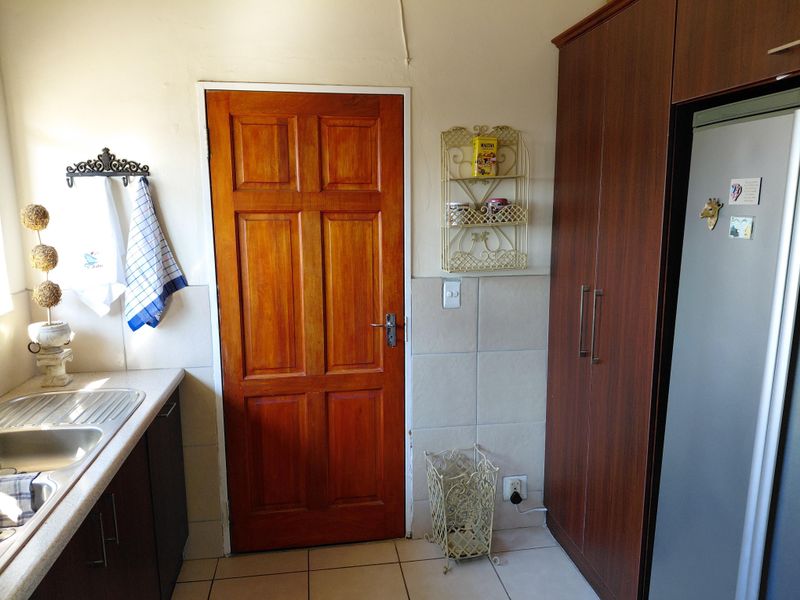 A functional kitchen area featuring built-in cabinetry, a stainless steel sink, tiled splashbacks, and a solid timber door.