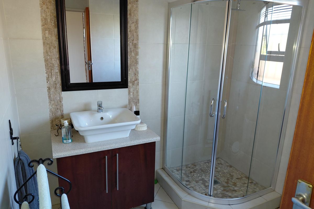 A functional bathroom featuring a corner shower enclosure, a modern vessel sink set on a vanity cabinet, and neutral wall tiling.