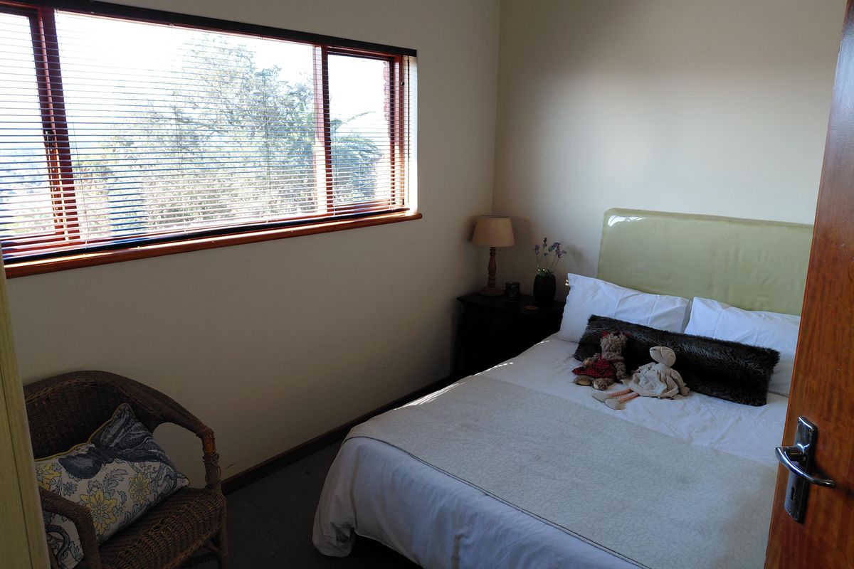 A cozy bedroom featuring carpeted flooring and a large window with timber frames and horizontal blinds, offering natural light and exterior views.