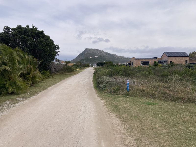 A view of an unpaved residential road leading towards a mountain, showcasing the surrounding landscape and nearby residential properties.