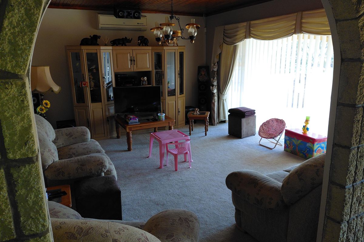 A spacious living room featuring a timber-paneled ceiling, a stone-clad archway entrance, and a wall-mounted air conditioning unit.