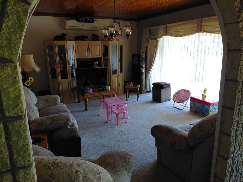 A spacious living room featuring a timber-paneled ceiling, a stone-clad archway entrance, and a wall-mounted air conditioning unit.