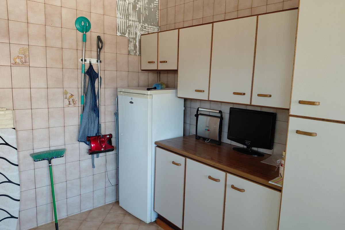 A dated kitchen area featuring tiled walls, laminate cabinetry, and a wood-look countertop, requiring cosmetic updates to improve functionality and aesthetic appeal.