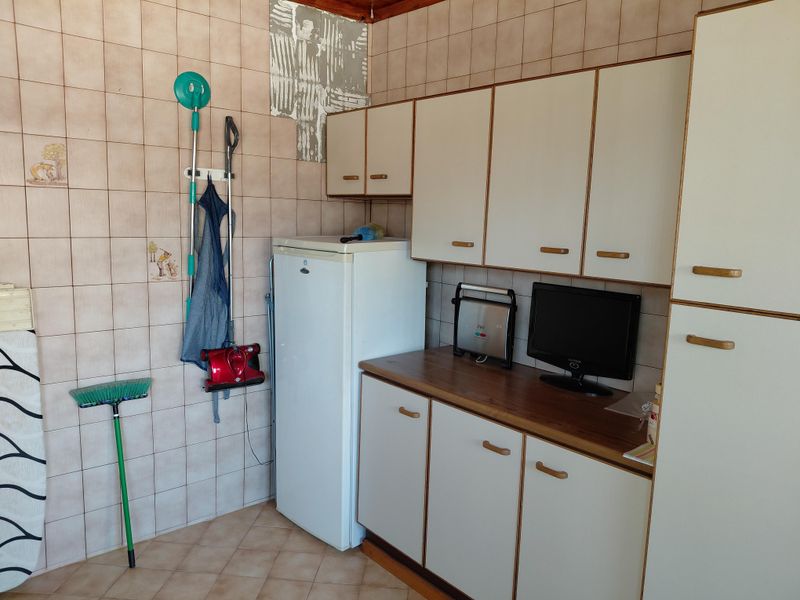 A dated kitchen area featuring tiled walls, laminate cabinetry, and a wood-look countertop, requiring cosmetic updates to improve functionality and aesthetic appeal.