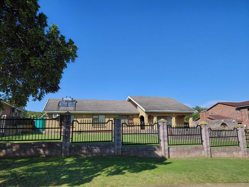 Front view of a single-story brick house featuring a tiled roof, solar water heating system, and a secure perimeter wall with metal fencing.