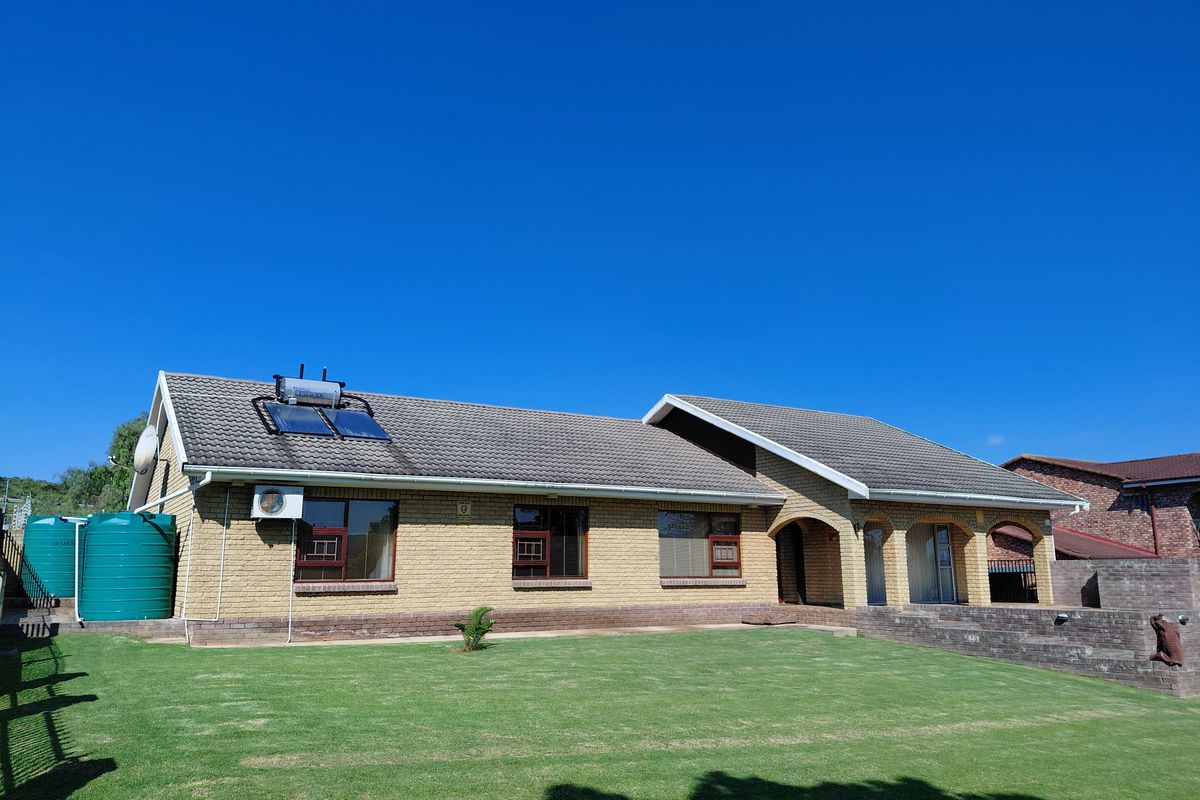 Rear view of a brick house featuring a tiled roof, solar water heating system, air conditioning unit, water storage tanks, and a covered patio area.