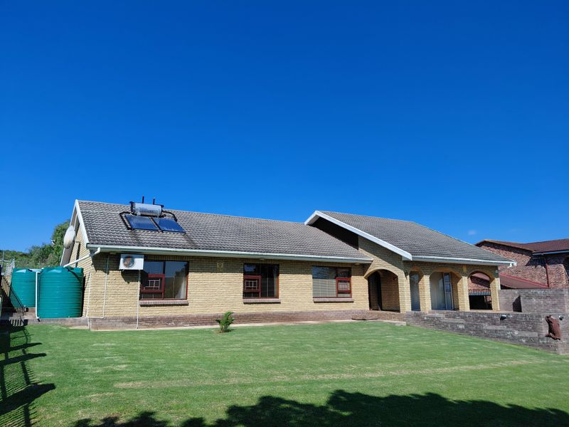 Rear view of a brick house featuring a tiled roof, solar water heating system, air conditioning unit, water storage tanks, and a covered patio area.