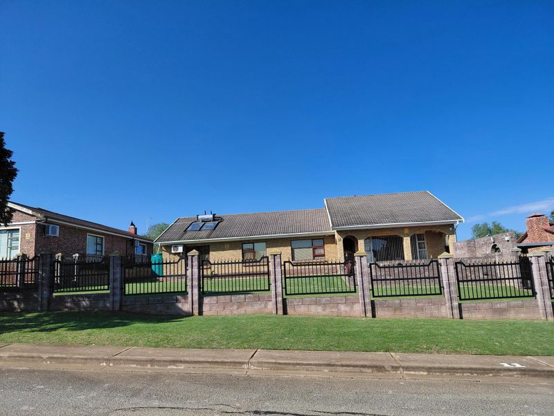 Front view of a single-story brick house featuring a tiled roof, solar water heater, and a secure perimeter wall with metal fencing.
