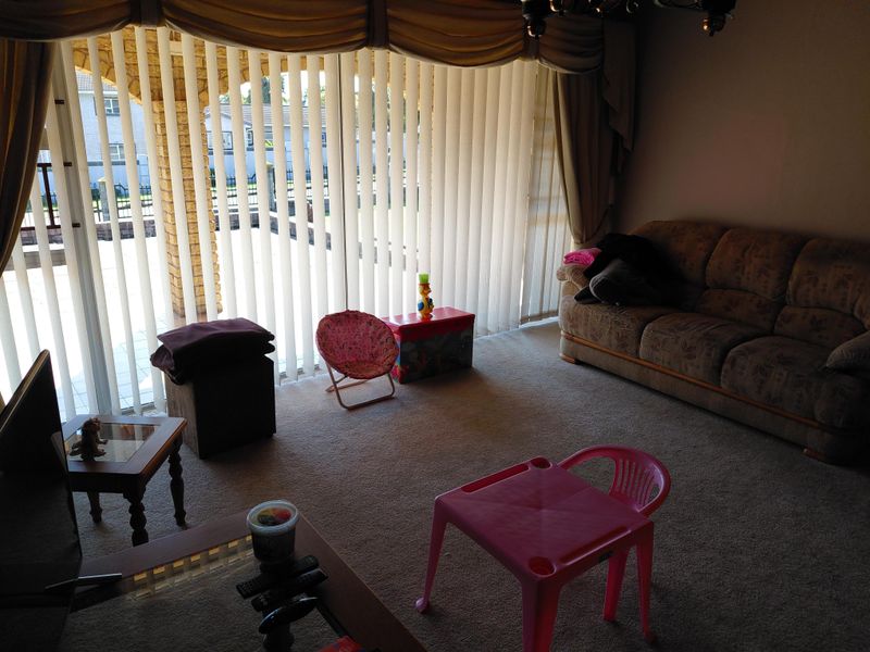 A living room featuring carpet flooring and large sliding glass doors with vertical blinds, providing access to an outdoor patio area.