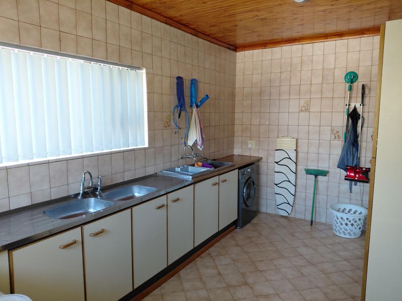 Functional laundry room featuring tiled walls, timber ceiling, double stainless steel sink, and built-in cabinetry with space for a washing machine.