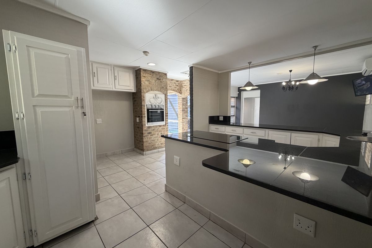 Spacious kitchen featuring granite countertops, built-in oven, and an exposed brick feature wall, flowing into an open-plan living area with tiled flooring.