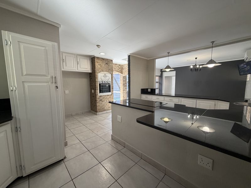 Spacious kitchen featuring granite countertops, built-in oven, and an exposed brick feature wall, flowing into an open-plan living area with tiled flooring.