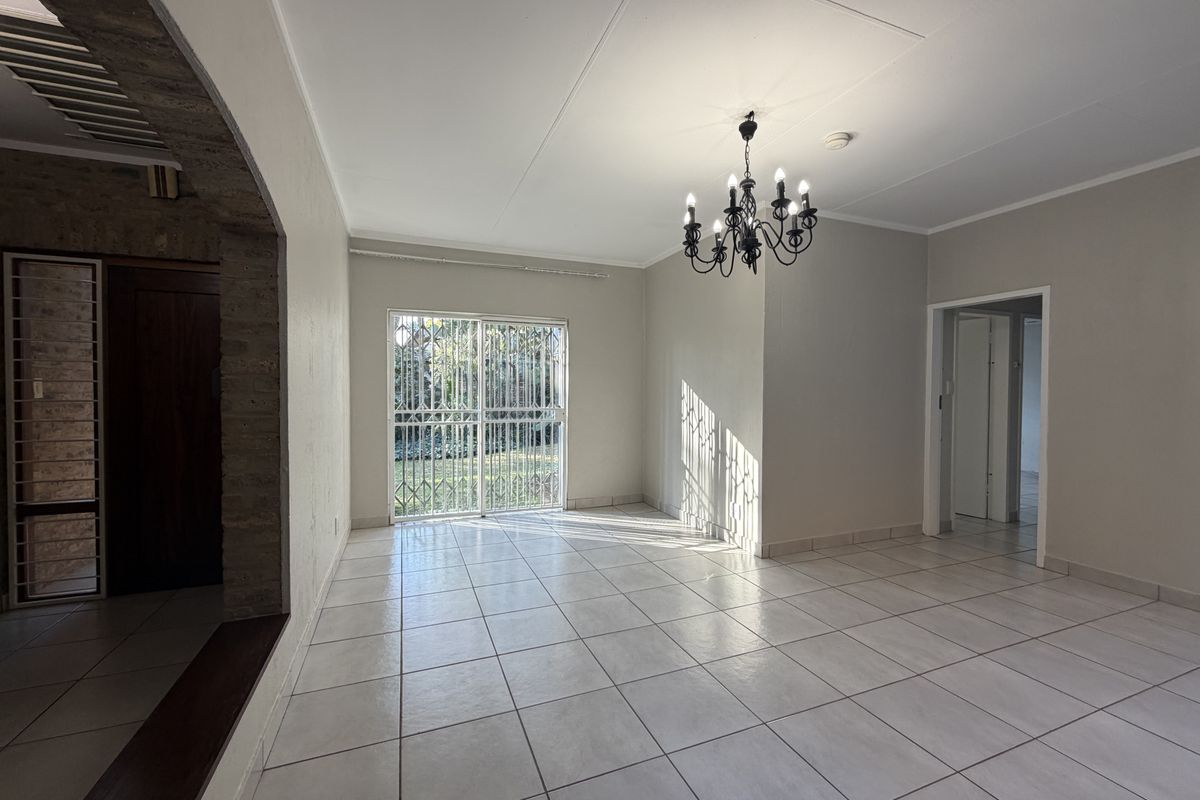 A bright, empty living room featuring neutral ceramic floor tiles, an exposed brick archway, and a decorative wrought iron chandelier with access to the garden.