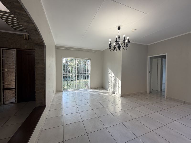 A bright, empty living room featuring neutral ceramic floor tiles, an exposed brick archway, and a decorative wrought iron chandelier with access to the garden.