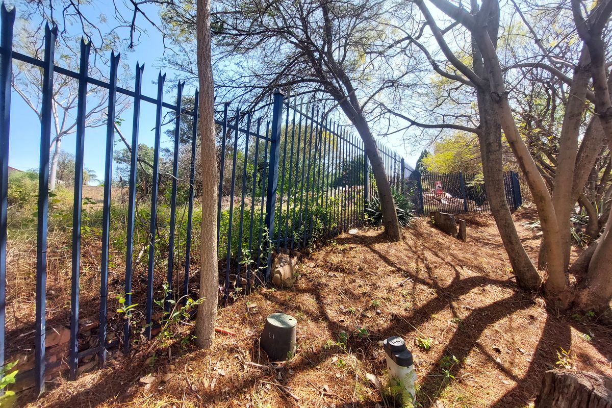 A view of the property boundary featuring steel palisade fencing and mature trees on a sloped residential plot.