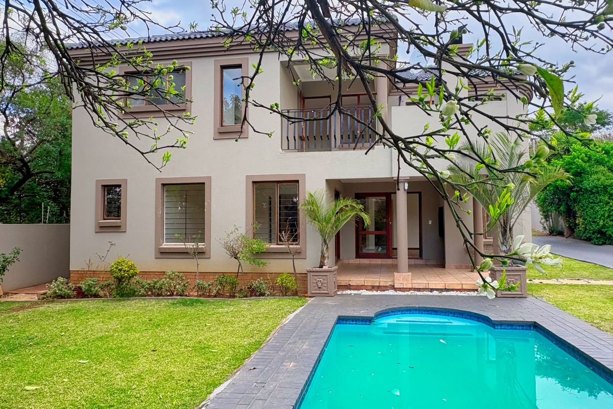 Rear view of a two-story house featuring a swimming pool, paved patio area, balcony, and well-maintained garden.