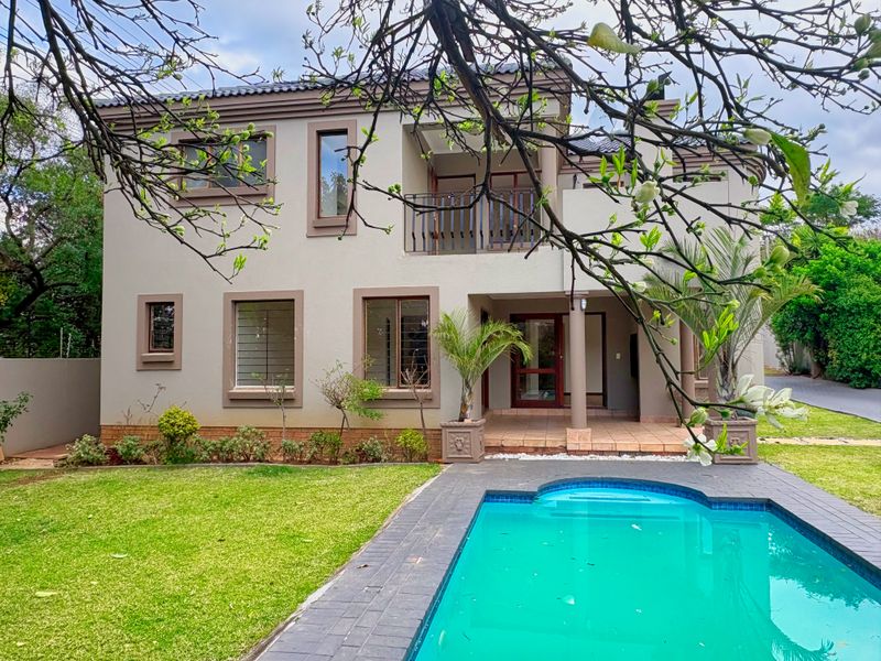 Rear view of a two-story house featuring a swimming pool, paved patio area, balcony, and well-maintained garden.