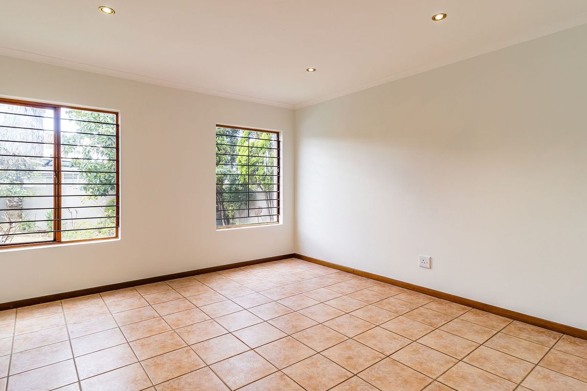 A bright, empty bedroom featuring neutral walls, tiled flooring, and windows fitted with security bars.