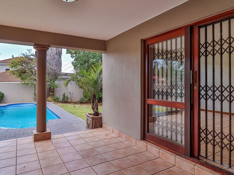 A covered patio area featuring tiled flooring and a structural column, providing direct access to the swimming pool and garden.