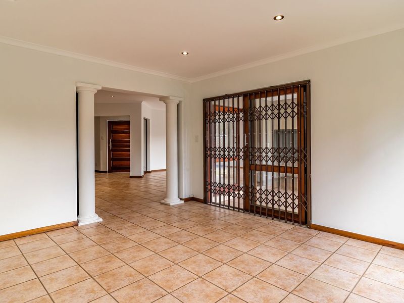 Spacious living area featuring ceramic floor tiles, decorative columns, and a secure sliding glass door leading to the exterior.