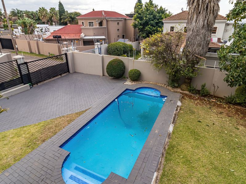 An elevated view of a private swimming pool area featuring paved surrounds, perimeter walling with electric fencing, and a secure driveway entrance.