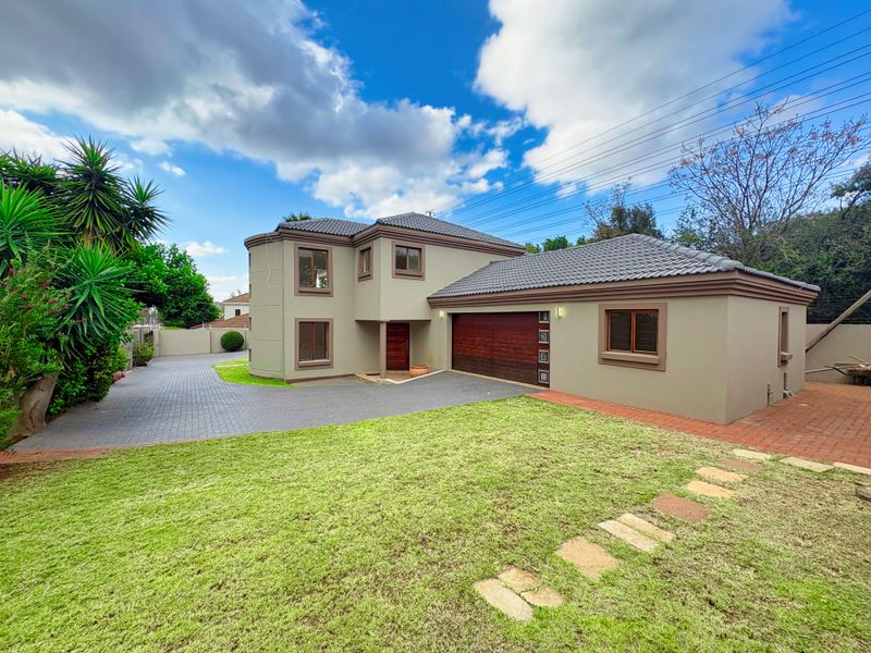 A well-maintained double-story residential property featuring a paved driveway, double garage with wooden door, and a neat front lawn with stone pathway.