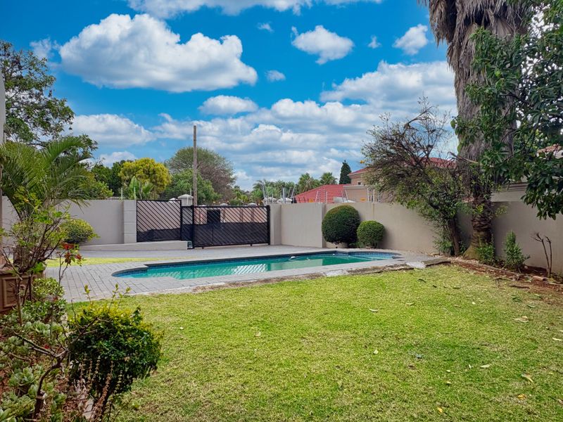 A private outdoor pool area featuring a paved deck, perimeter boundary walls, and a well-maintained lawn.