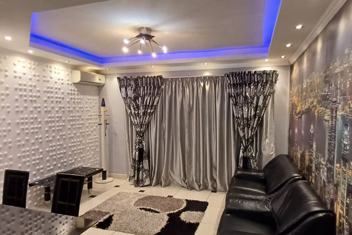 Living room featuring a recessed ceiling with blue LED accent lighting, a textured feature wall, and split-system air conditioning.
