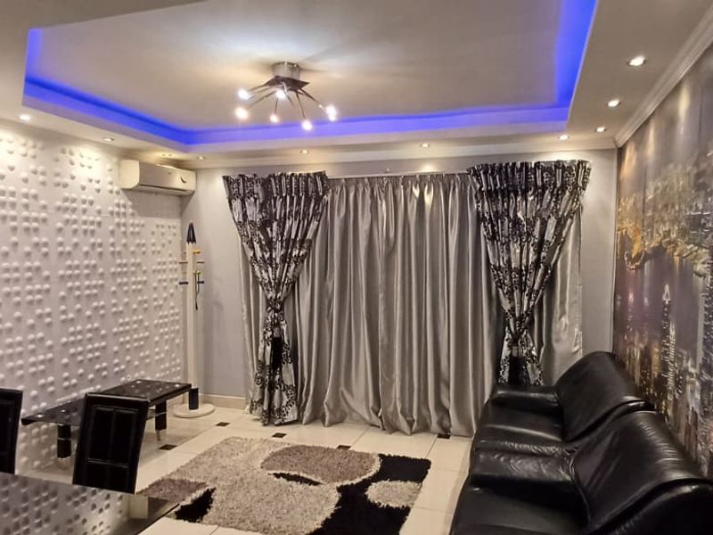 Living room featuring a recessed ceiling with blue LED accent lighting, a textured feature wall, and split-system air conditioning.