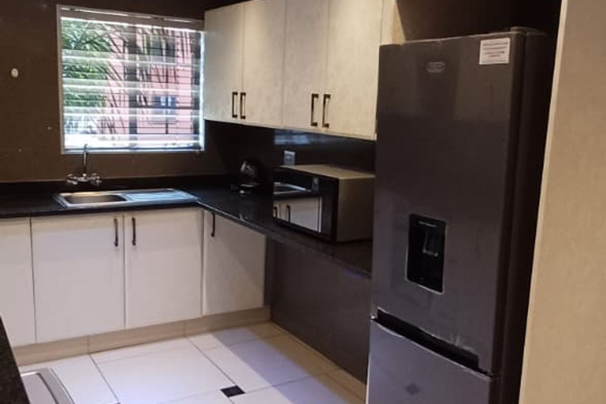 Modern kitchen featuring sleek white cabinetry, dark granite countertops, tiled flooring with decorative accents, and recessed ceiling lighting.