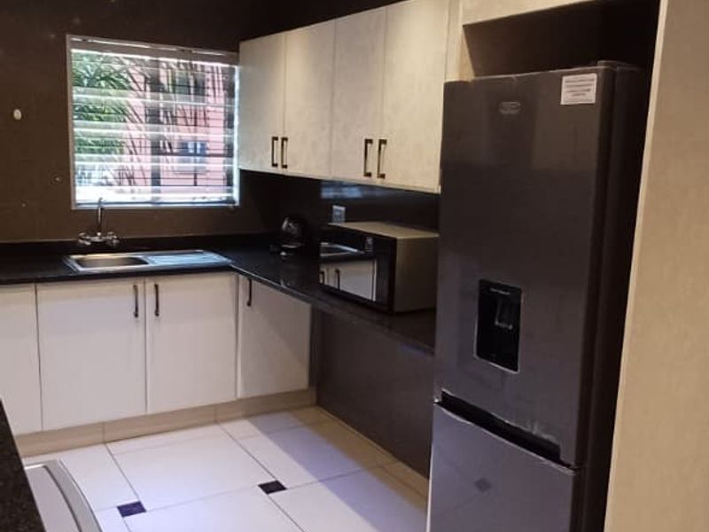 Modern kitchen featuring sleek white cabinetry, dark granite countertops, tiled flooring with decorative accents, and recessed ceiling lighting.