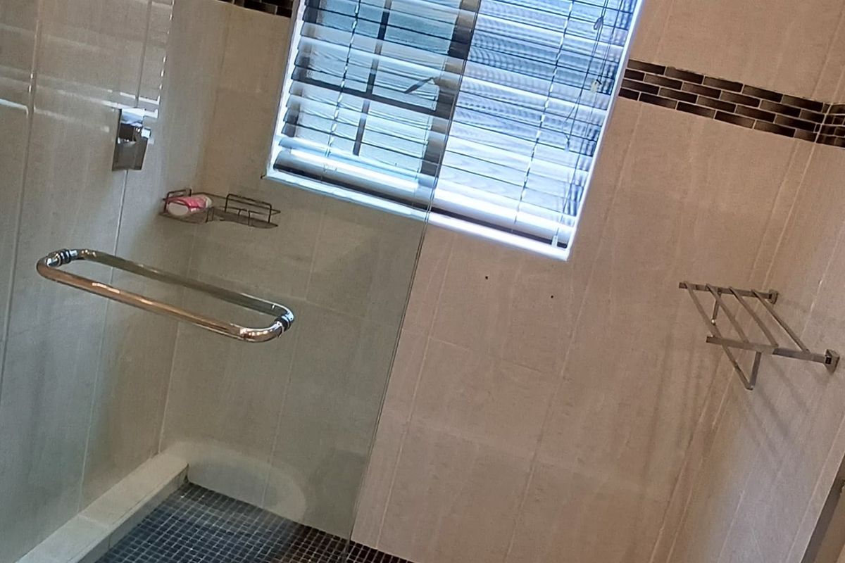 A modern bathroom featuring a glass-enclosed shower with dark mosaic floor tiling and neutral wall tiles.