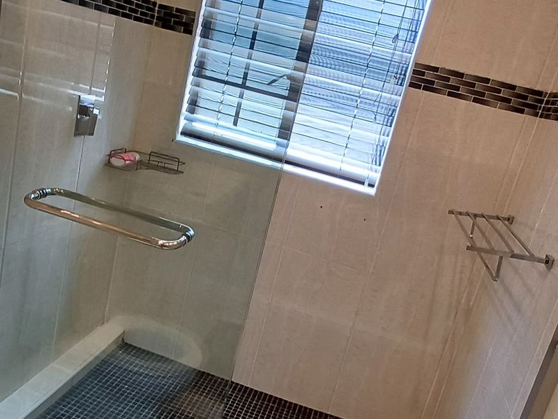 A modern bathroom featuring a glass-enclosed shower with dark mosaic floor tiling and neutral wall tiles.