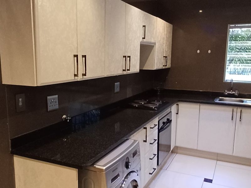 Modern kitchen featuring sleek white cabinetry, dark granite countertops, integrated oven and hob, and polished tiled flooring with decorative accents.