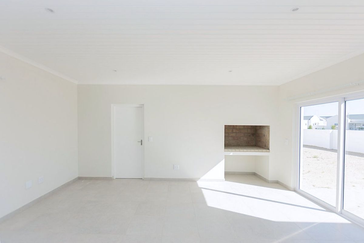 Bright and spacious living area featuring neutral tiled flooring, a built-in braai, and large sliding glass doors leading to the exterior.