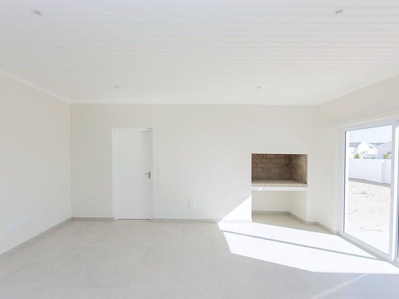 Bright and spacious living area featuring neutral tiled flooring, a built-in braai, and large sliding glass doors leading to the exterior.