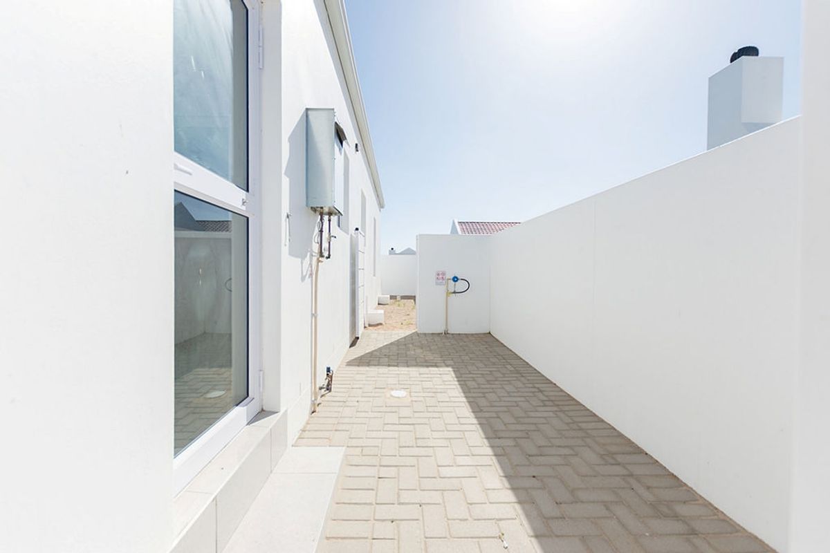 A clean, paved side passage or rear courtyard area featuring white boundary walls and an external gas geyser installation.