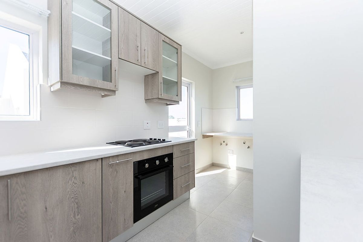 Modern kitchen featuring light wood-grain cabinetry, stone countertops, built-in oven and hob, and clean tiled finishes in a bright, open layout.