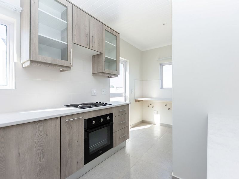 Modern kitchen featuring light wood-grain cabinetry, stone countertops, built-in oven and hob, and clean tiled finishes in a bright, open layout.