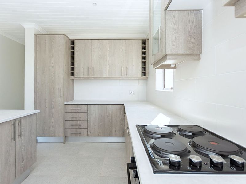 Modern kitchen featuring light wood-grain cabinetry, stone countertops, a built-in electric hob, and clean tiled splashbacks in a bright, neutral space.