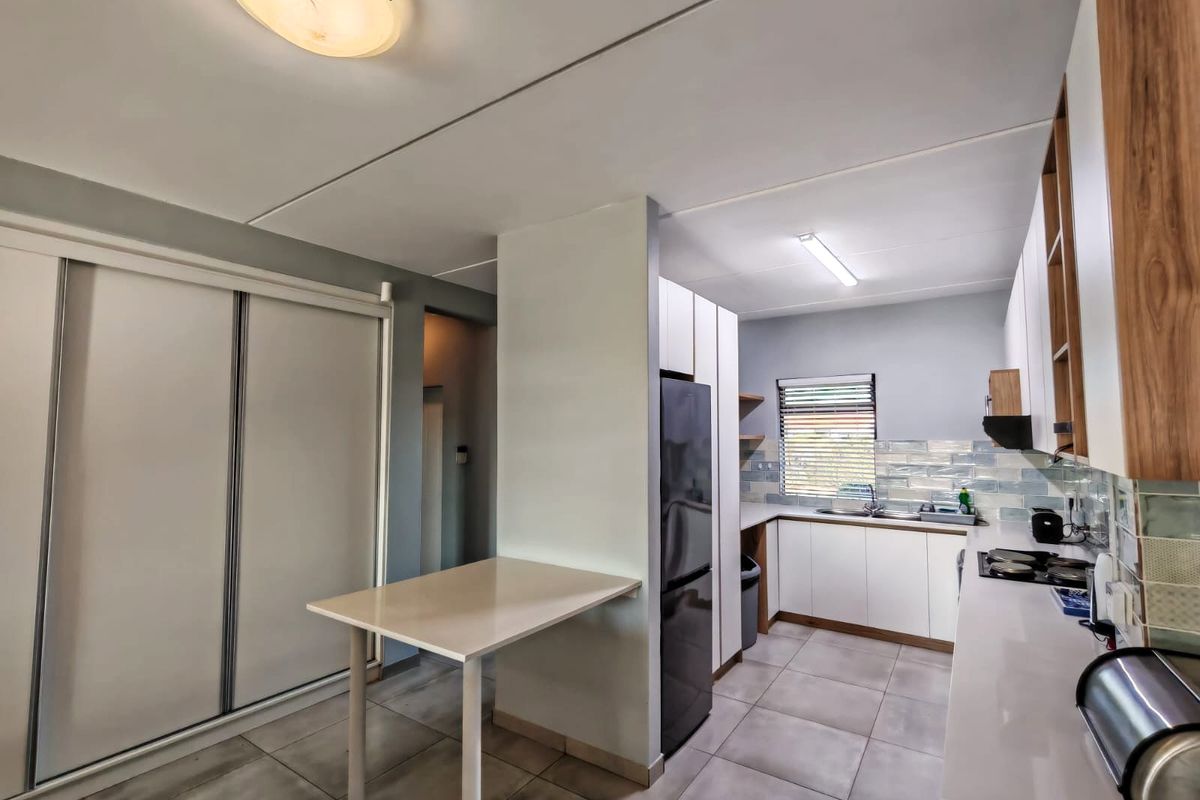 A modern kitchen featuring white cabinetry, tiled flooring, a built-in hob with extractor fan, and a functional breakfast nook area.