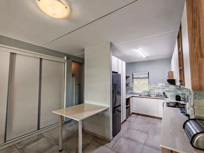 A modern kitchen featuring white cabinetry, tiled flooring, a built-in hob with extractor fan, and a functional breakfast nook area.