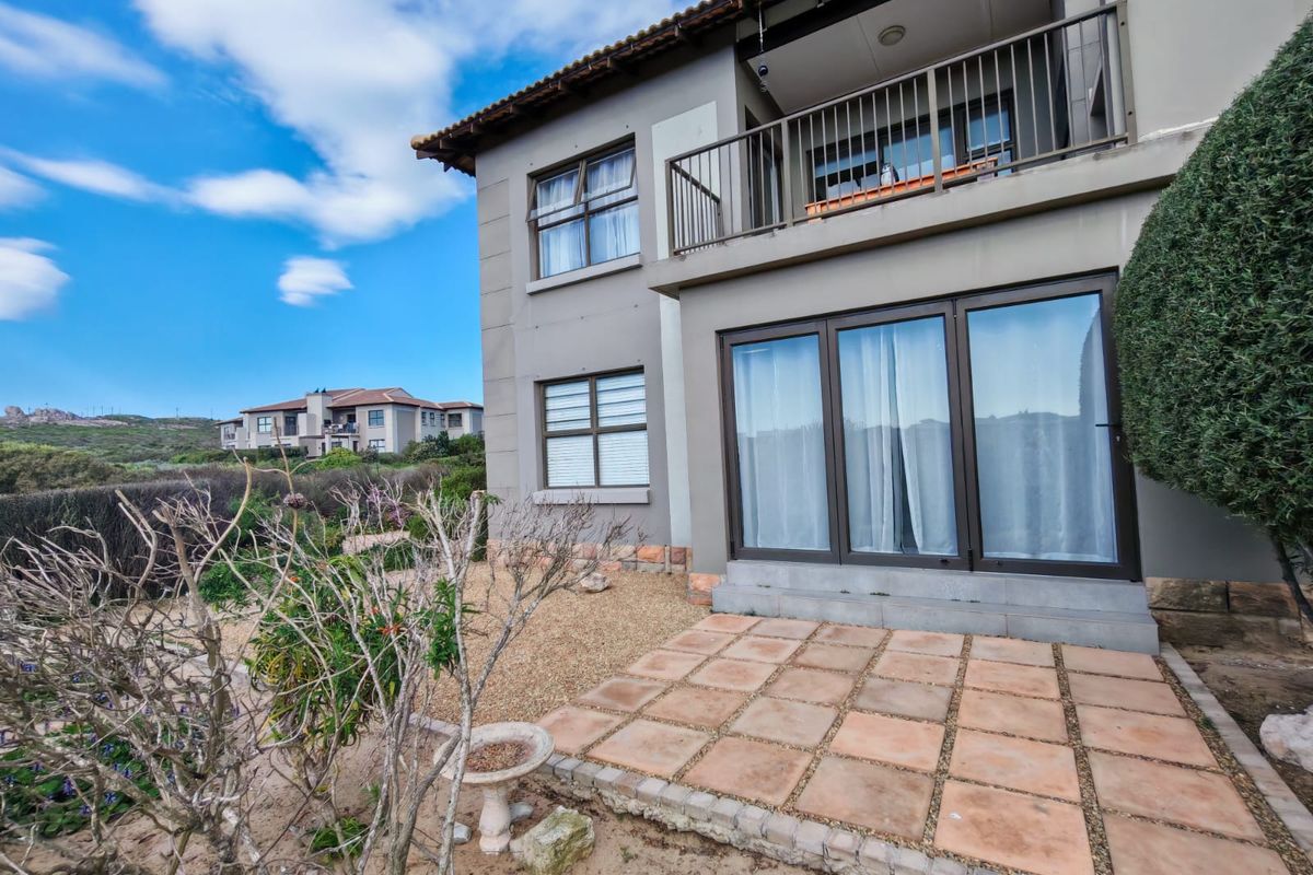 Rear view of the apartment featuring a ground-level tiled patio, upper-level balcony with metal railing, and large sliding glass doors.