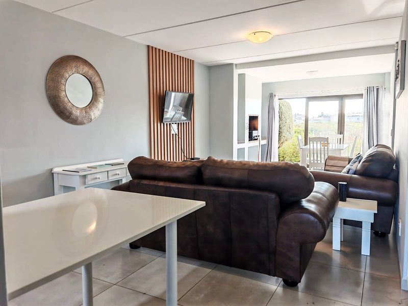 Open-plan living area featuring tiled floors, a decorative slatted timber wall, and sliding glass doors leading to an outdoor patio with a built-in braai.