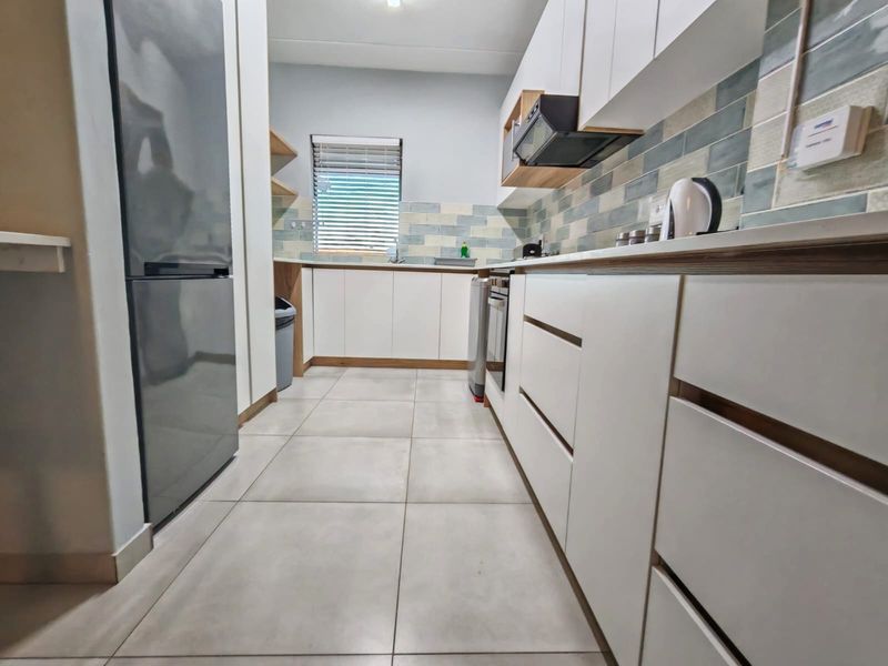 Modern kitchen featuring clean white cabinetry, tiled backsplash, built-in oven with extractor fan, and neutral floor tiles.