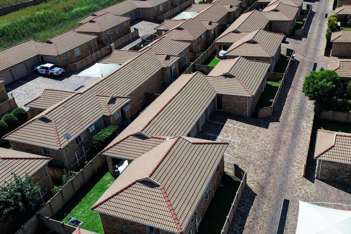 Aerial view of a townhouse complex featuring multiple units with tiled roofs, brick-paved driveways, and private garden spaces.