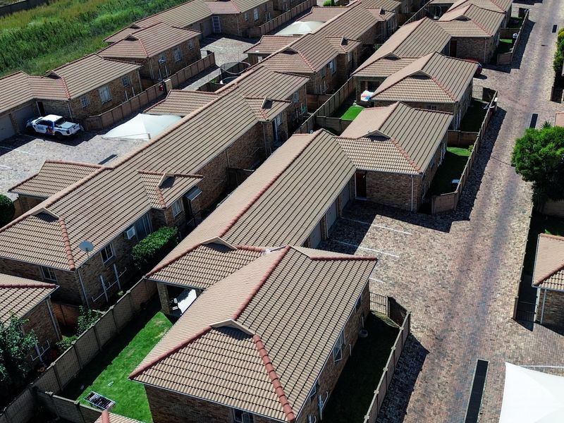 Aerial view of a townhouse complex featuring multiple units with tiled roofs, brick-paved driveways, and private garden spaces.