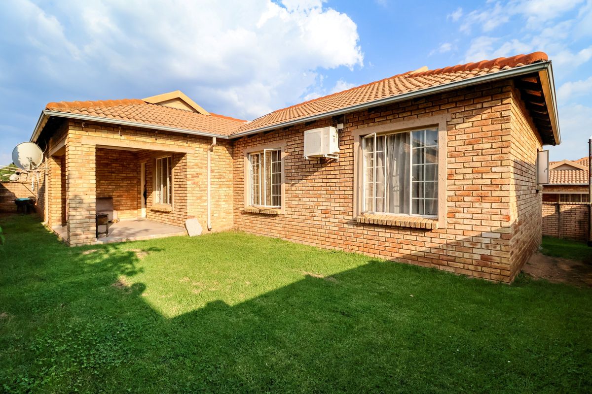 Rear view of the townhouse featuring a face brick exterior, tiled roof, and a covered patio area overlooking a private garden.