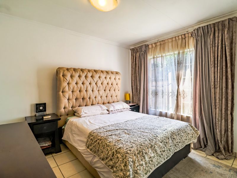 A cozy bedroom featuring tiled flooring and large windows with full-length curtains, providing natural light and a comfortable living space.